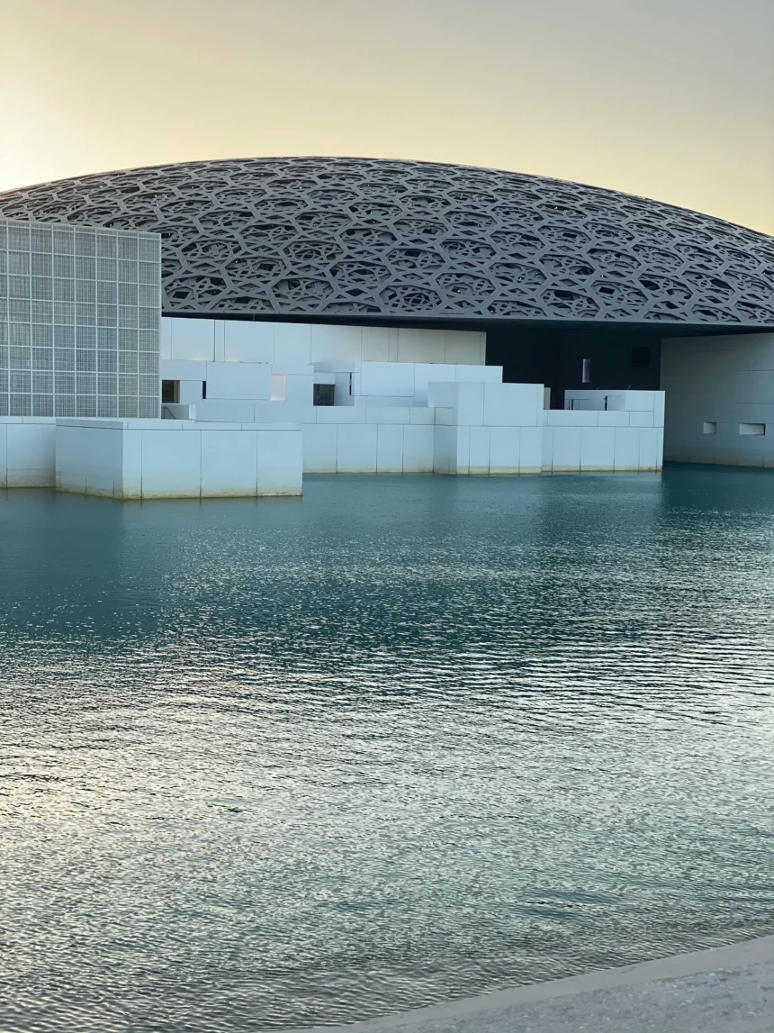 Louvre Abu Dhabi, a stunning modern museum with a geometric dome, reflecting on the calm waters of Saadiyat Island.