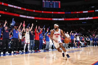 Detroit Pistons player driving with ball as home crowd cheers at Little Caesars Arena